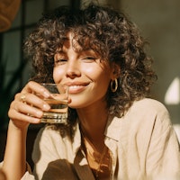 Femme aux cheveux bouclés souriant, un verre d'eau à la main, en lumière naturelle