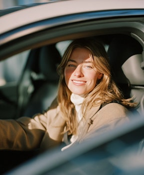 Femme souriante au volant d’une voiture moderne, dans une lumière naturelle chaleureuse