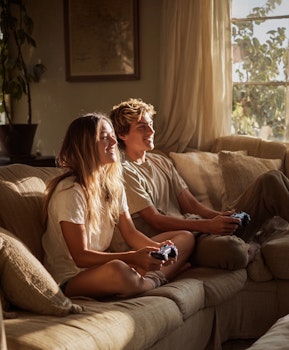 Deux jeunes joueurs souriants devant une console de jeu, assis sur un canapé dans un salon lumineux